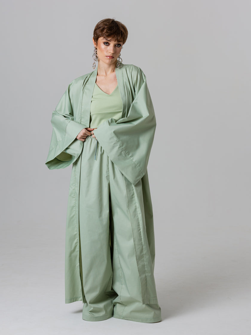 Woman wearing a light green abaya against a plain background