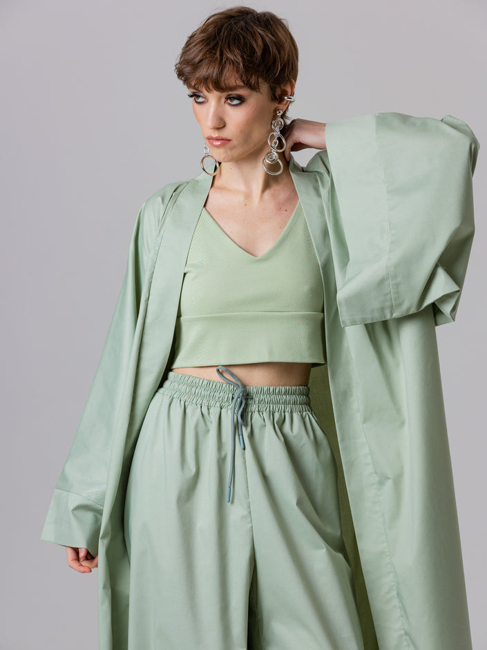 Woman wearing a light green outfit with a matching coat against a plain background