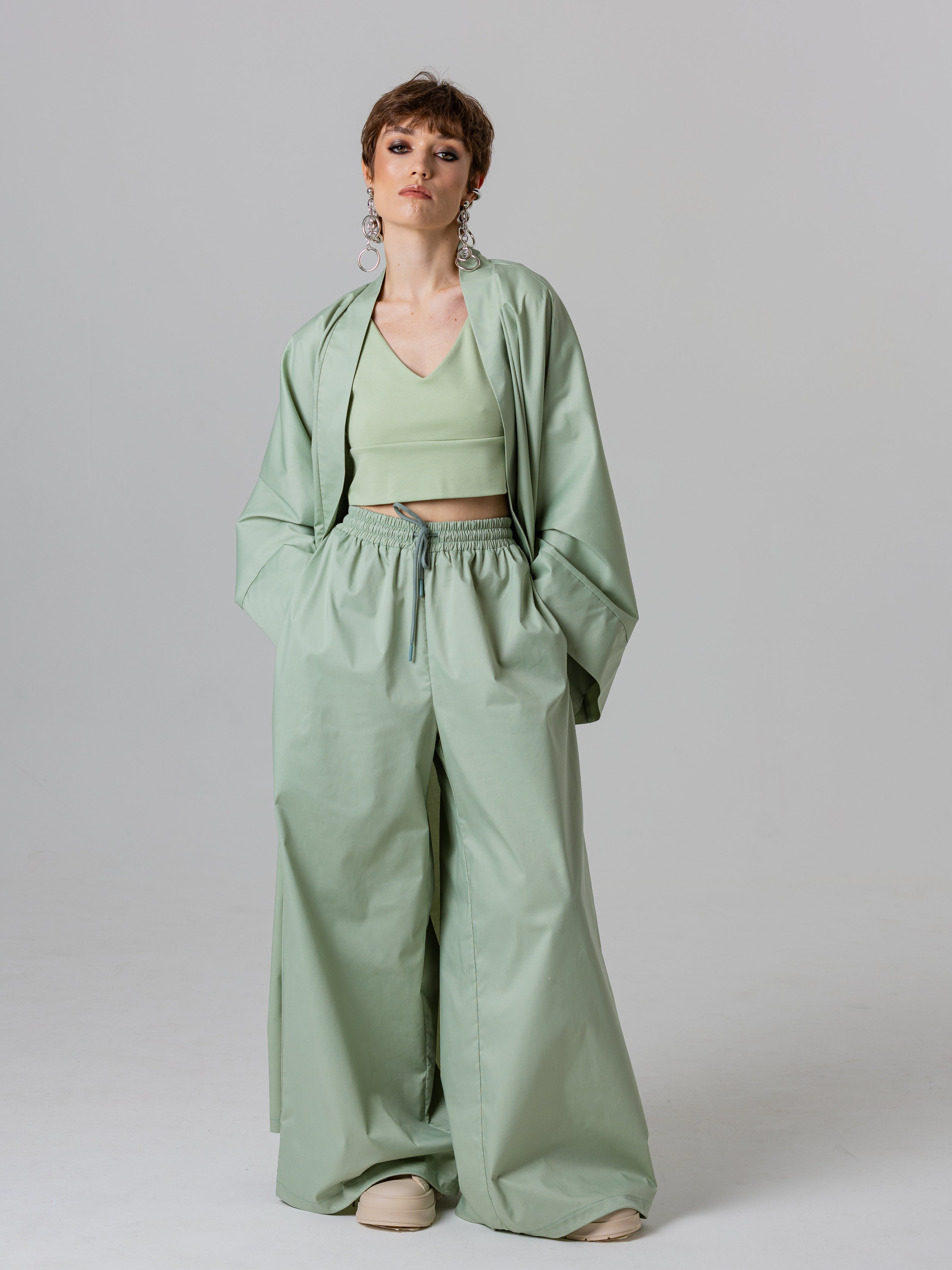 Woman wearing a green outfit with a jacket, top, and wide-leg pants on a plain background