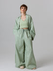 Woman wearing a green outfit with a jacket, top, and wide-leg pants on a plain background