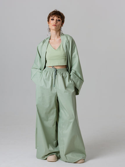 Woman wearing a green outfit with a jacket, top, and wide-leg pants on a plain background
