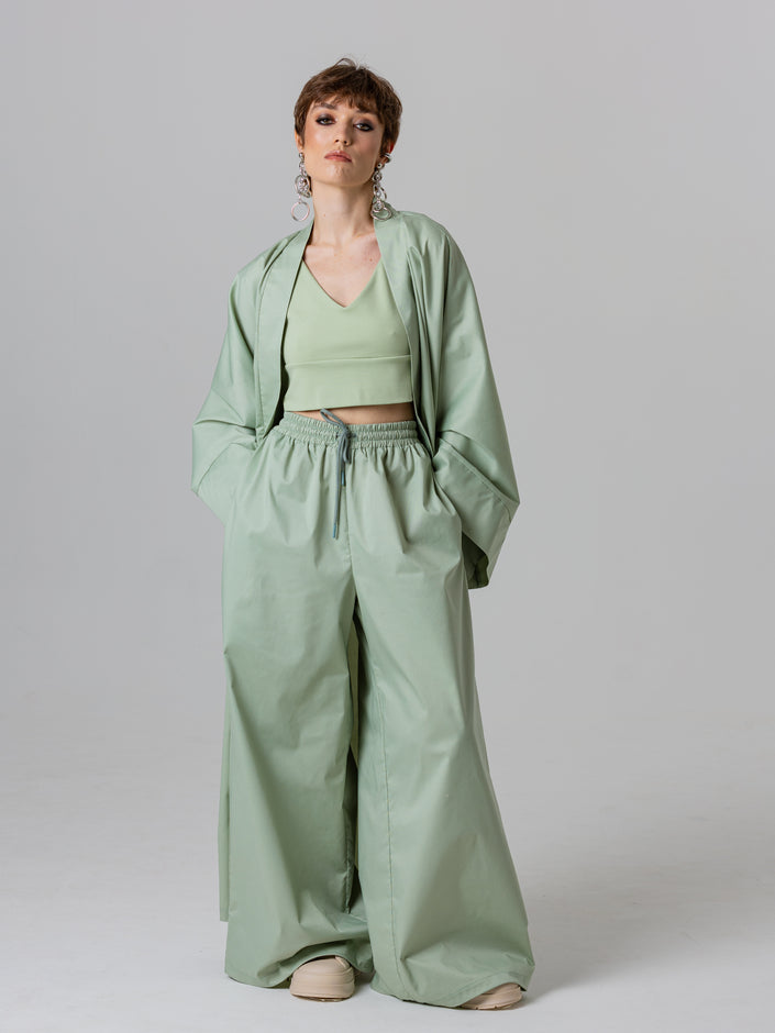 Woman wearing a green outfit with a jacket, top, and wide-leg pants on a plain background